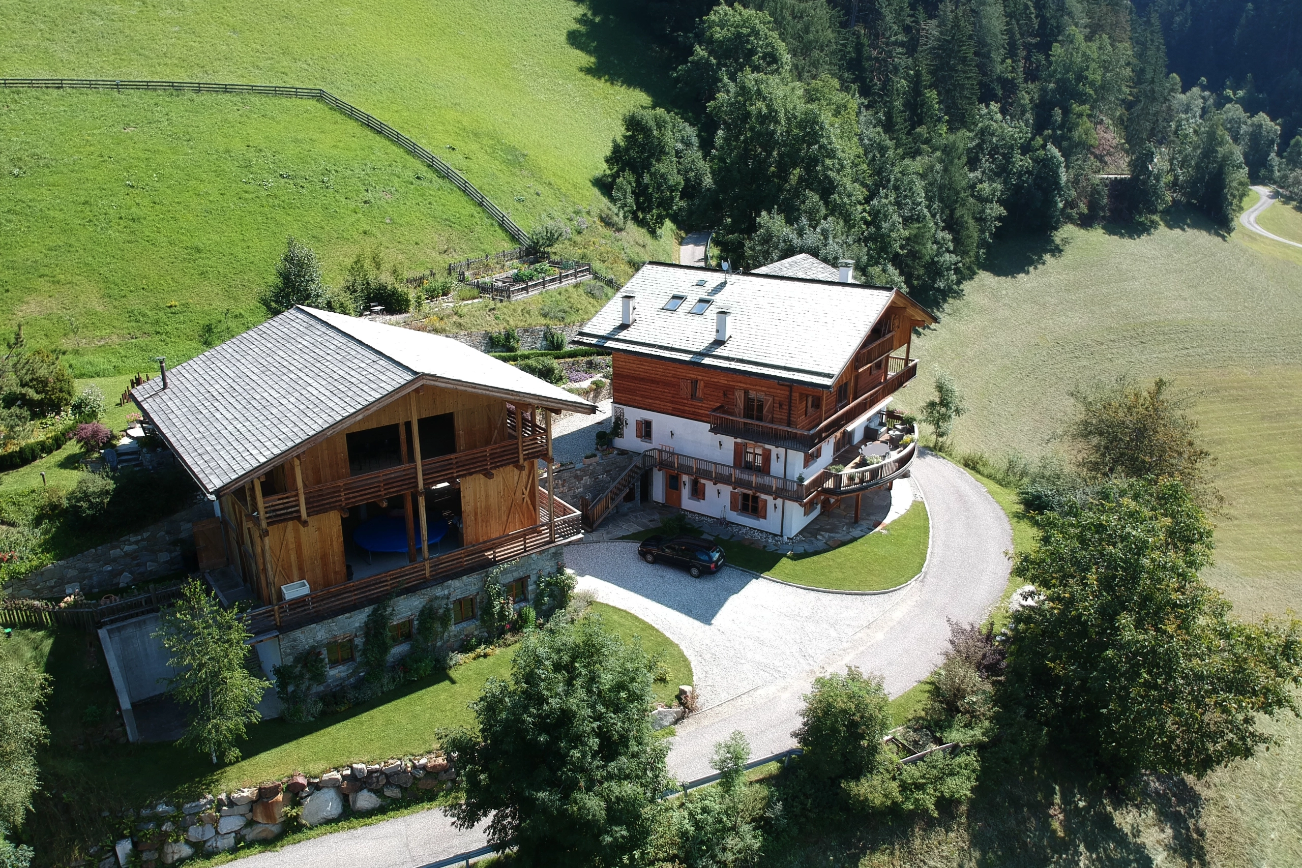 Perfect Hideaways real estate property: An aerial view of adjacent chalets in the Italian countryside, featuring views of the Dolomite mountain range. Ragginerhof, Italy.