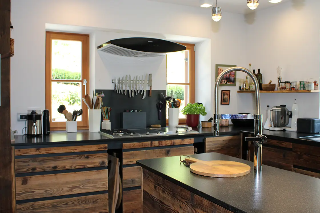 Perfect Hideaways real estate property: A kitchen area, featuring rustic wooden drawers and shutter windows, while dark countertops in a contemporary style balances the Italian home style, with its German engineering. Ragginerhof, Italy.