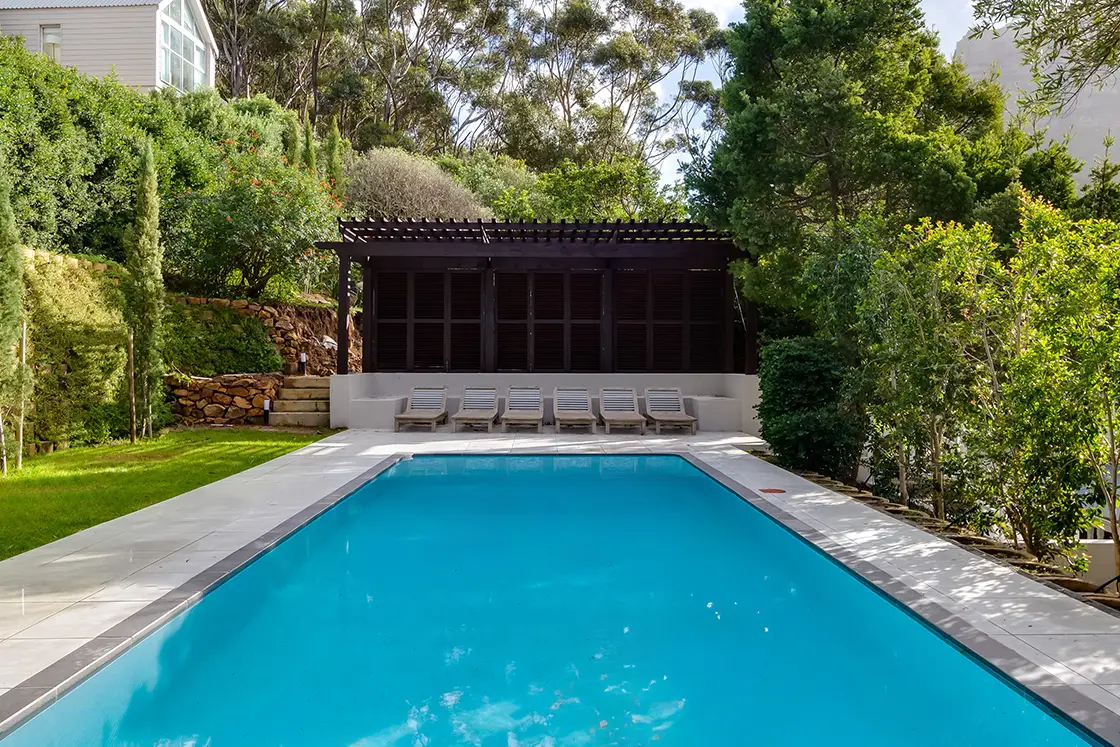 Perfect Hideaways real estate property: A pool surrounded by flagstone tiles above the main house, with sun loungers under a patio on one end, and a garden. The Berg Manor and Villas, Hout Bay.