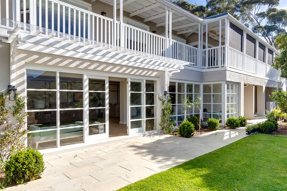 Perfect Hideaways real estate property: A double-story house with French pane windows, outside the lounge is a patio with flagstone pavers, featuring planting areas on either side of the lounge doors. The Berg Manor and Villas, Hout Bay.