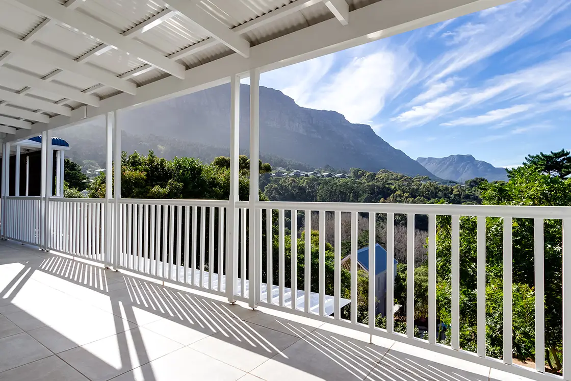 Perfect Hideaways real estate property: The second-floor balcony has expansive views of the mountains, featuring all white tile floors, balcony railing, and corrugated steel ceiling which is supported by wooden beams. The Berg Manor and Villas, Hout Bay.