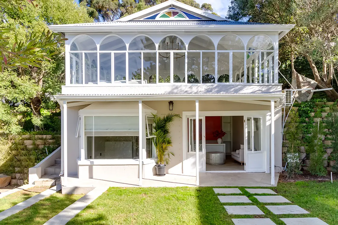 Perfect Hideaways real estate property: A double-story villa near the manor house, featuring a landscaped lawn with large pavers forming a walkway in the grass. The second floor has arched pane windows and a painted glass detail. The Berg Manor and Villas, Hout Bay.