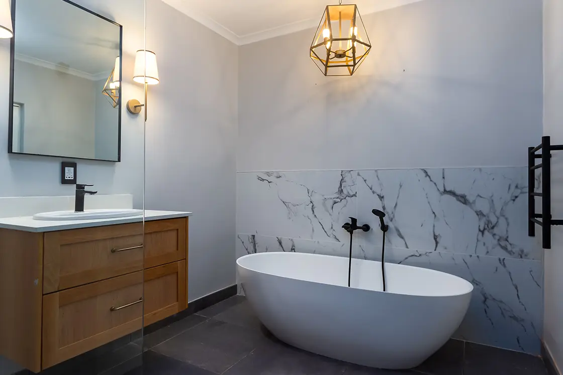 Perfect Hideaways real estate property: An en-suite bathroom with a bathtub and shower, featuring modern lighting, a basin unit, and a marble backsplash behind the bath. The Berg Manor and Villas, Hout Bay.