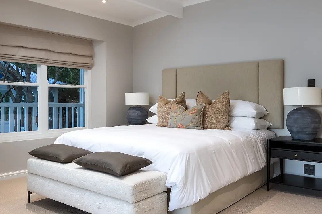 Perfect Hideaways real estate property: A bedroom with a double bed and ottoman, featuring dark-wood side tables and ceramic bedside lights. The Berg Manor and Villas, Hout Bay.