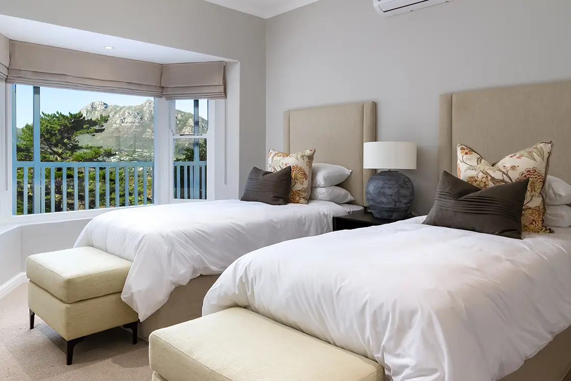 Perfect Hideaways real estate property: A bedroom with two single beds and an alcove window, featuring a view of the mountains through the bedroom window. The Berg Manor and Villas, Hout Bay.