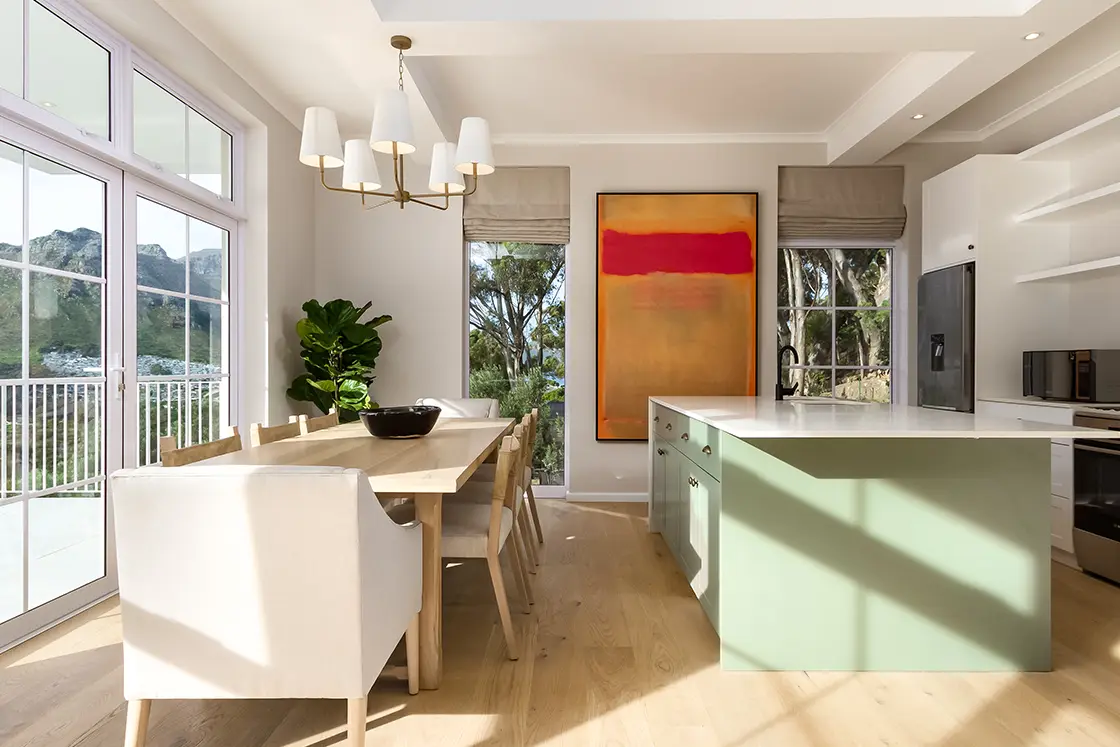 Perfect Hideaways real estate property: A living area with a dining area and kitchen, featuring a green kitchen island and wood floors. The Berg Manor and Villas, Hout Bay.