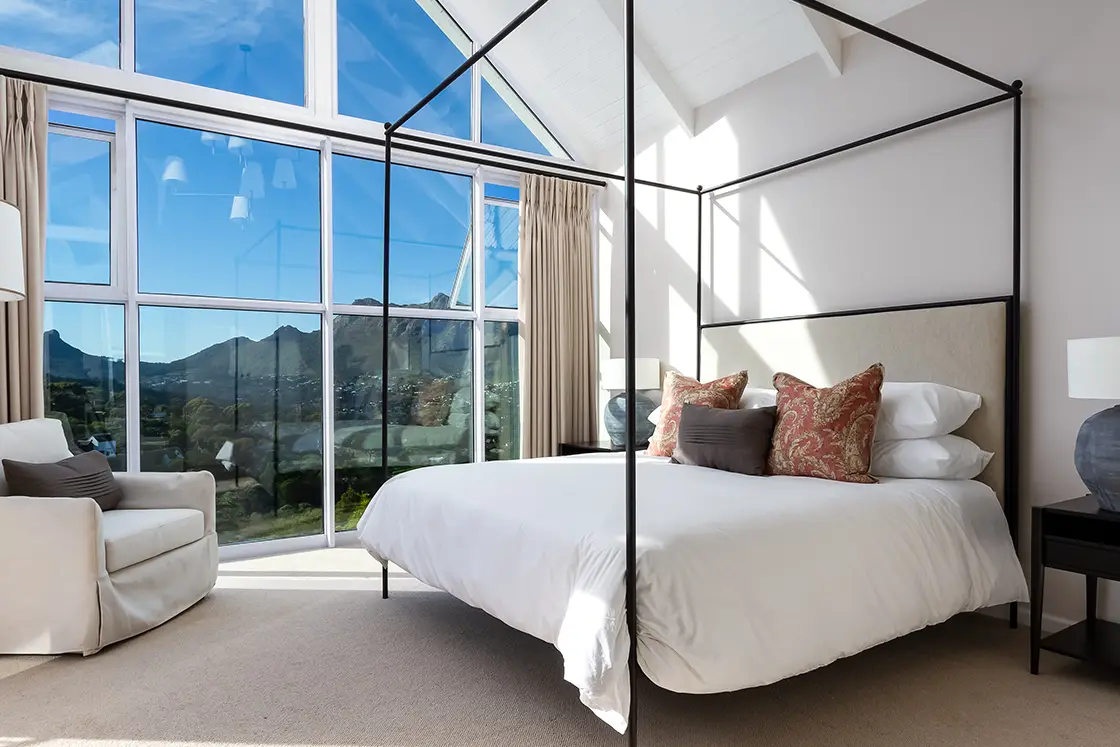 Perfect Hideaways real estate property: A bedroom with a steel four-poster bed, carpeted floors and a floor-to-ceiling paned window. The Berg Manor and Villas, Hout Bay.