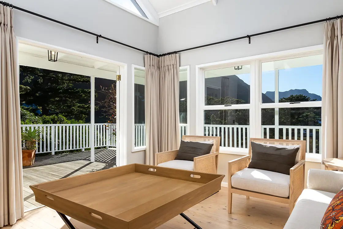 Perfect Hideaways real estate property: A living area with wooden decor to match the floor, as well as open doors leading to a wooden deck with white railings. The Berg Manor and Villas, Hout Bay.