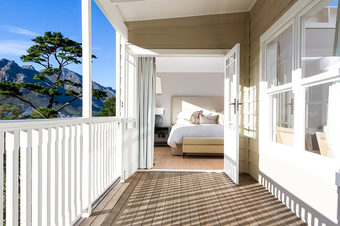 Perfect Hideaways real estate property: A bedroom with open doors onto a balcony, featuring a wooden floor and white railings. The Berg Manor and Villas, Hout Bay.