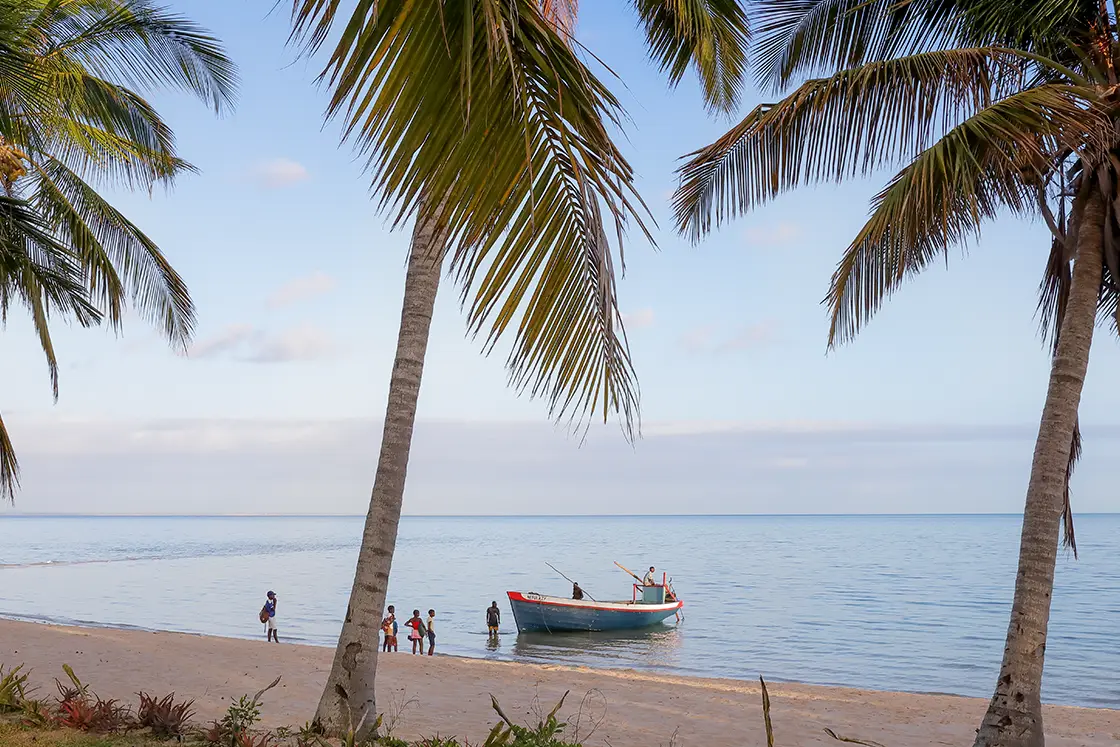 Perfect Hideaways real estate property: A beach with a local fishing vessel and people in the shallows, nearby garden at the foot of a villa. Villa Tanga, Benguerra Island.