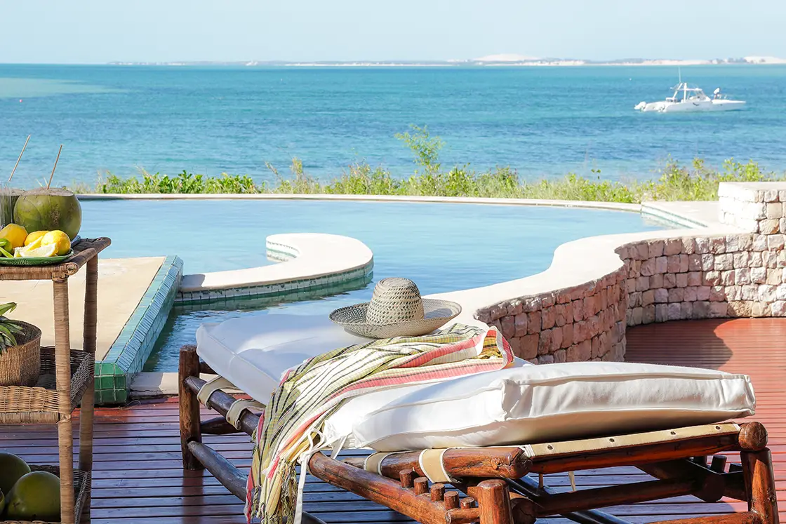 Perfect Hideaways real estate property: A poolside deck with sea views, featuring wooden sun loungers and a bar cart with fruit. Villa Tanga, Benguerra Island.