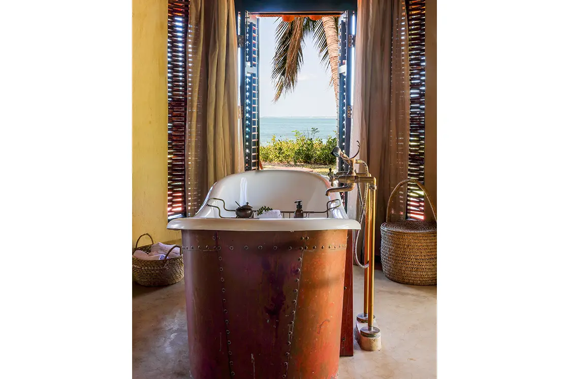 Perfect Hideaways real estate property: A bathroom with shuttered windows, featuring a central bathtub with industrial style elements. Villa Tanga, Benguerra Island.