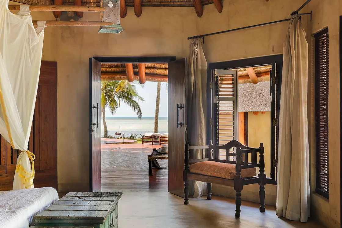 Perfect Hideaways real estate property: A bedroom area with an outdoor patio, featuring wood shutters and furniture in earth tones. Villa Tanga, Benguerra Island.