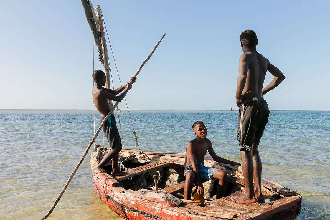 Perfect Hideaways real estate property: Three young local Mozambicans on a wooden fishing boat in shallow water. Villa Tanga, Benguerra Island.