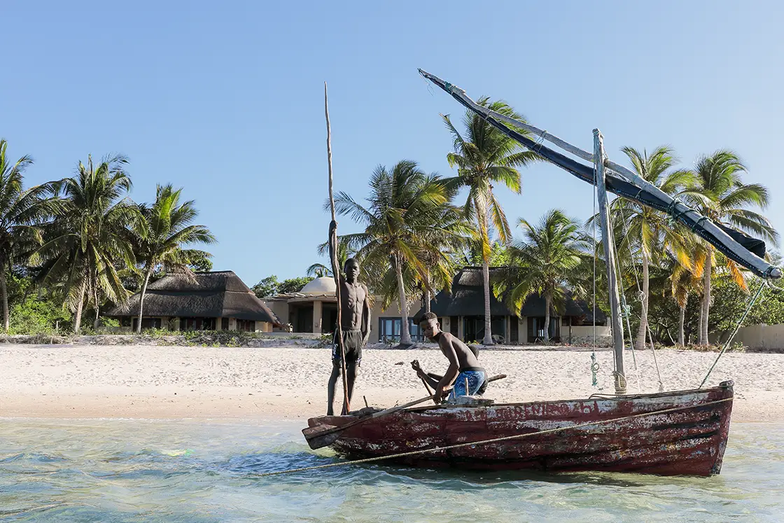 Perfect Hideaways real estate property: Two local Mozambicans on a fishing boat in the shallows, with a beachfront villa in the background. Villa Tanga, Benguerra Island.