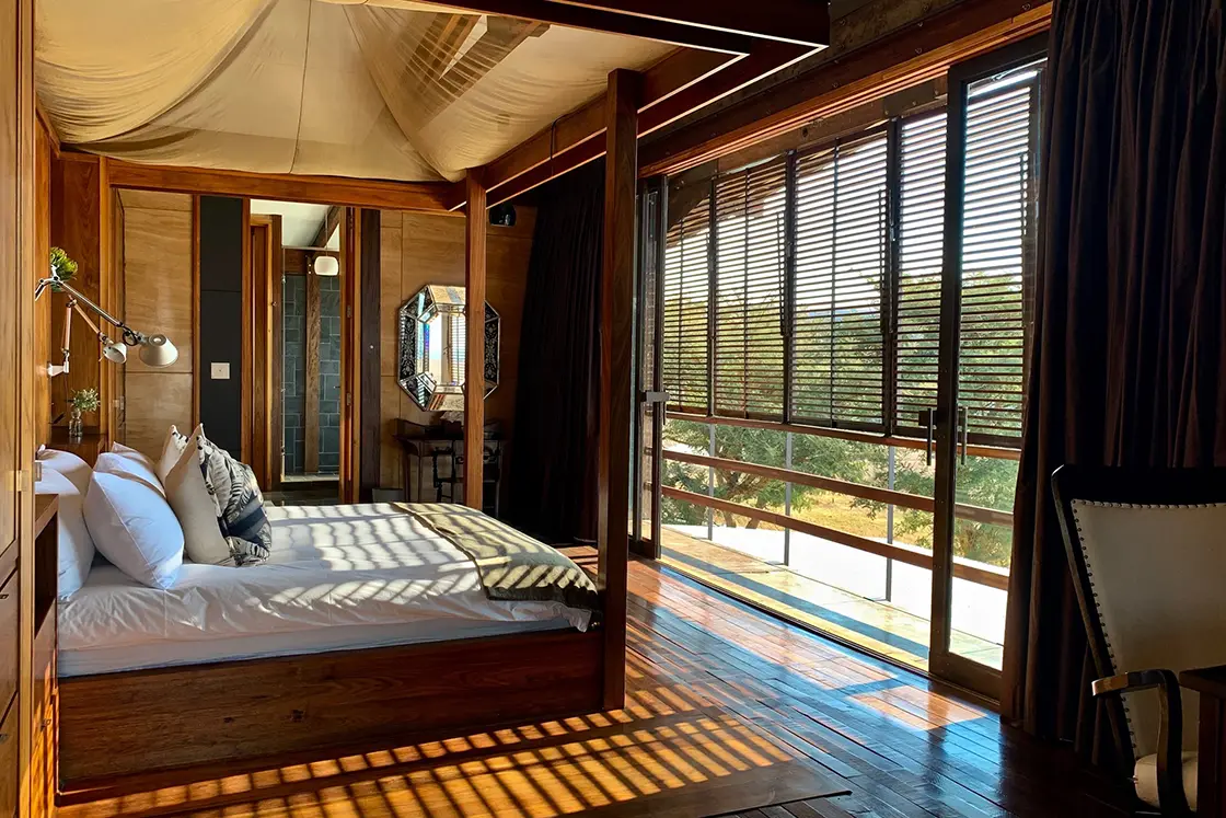 Perfect Hideaways real estate property: A bedroom with a wooden interior, featuring a four-poster bed, an en-suite bathroom, and a window with wooden shutters. Zulu Waters Game Reserve, Natal Midlands.