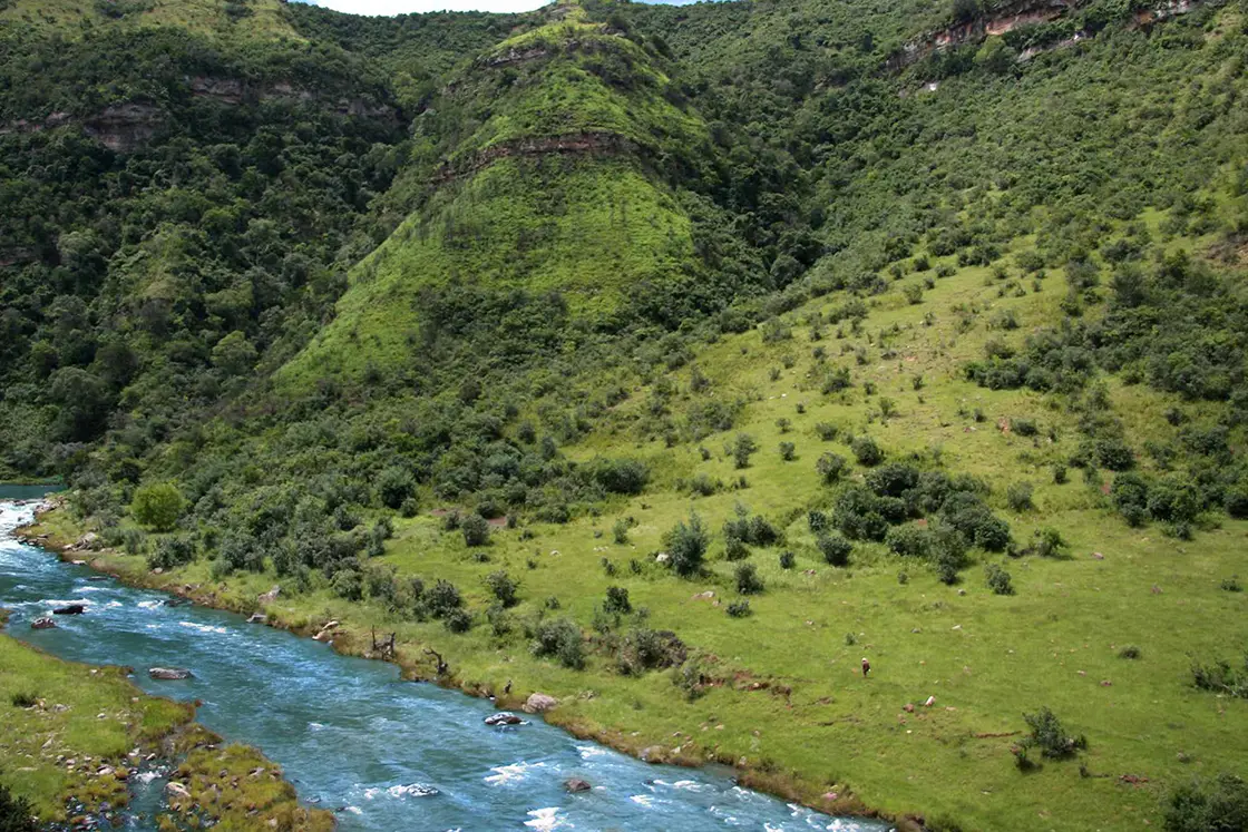 Perfect Hideaways real estate property: A river flows at the foot of a lush green hillside, a scenic feature of the game reserve. Zulu Waters Game Reserve, Natal Midlands.