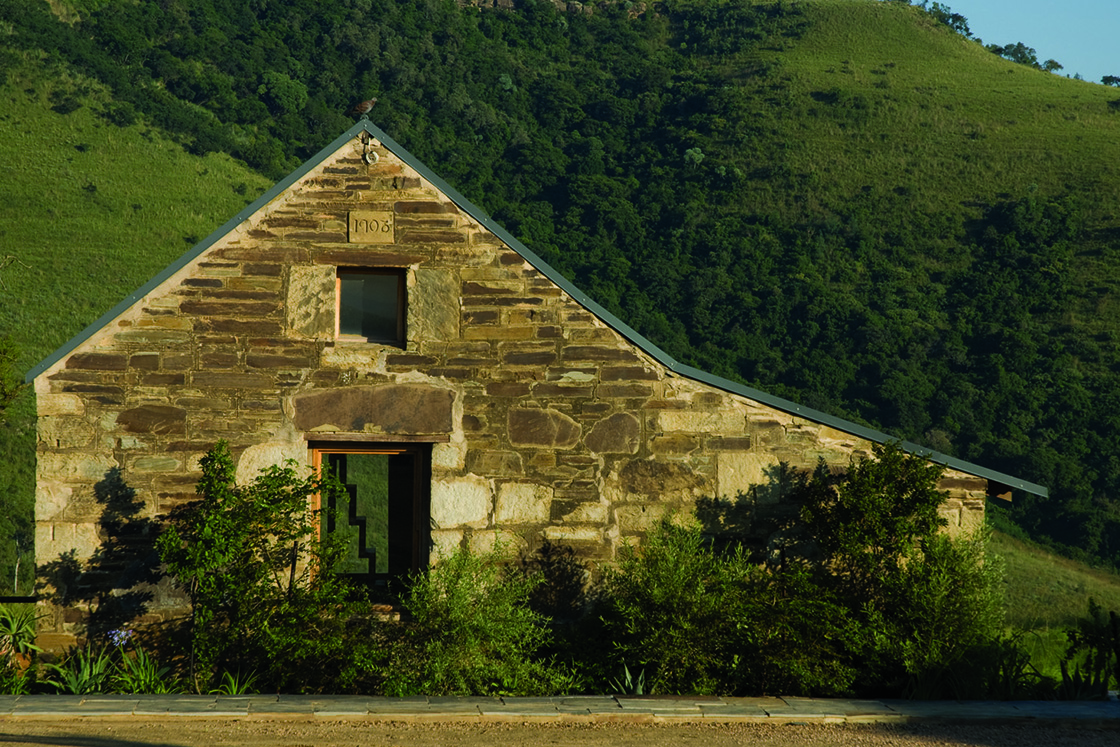 Perfect Hideaways real estate property: A small staff cottage beside the road leading to the guest lodges, featuring a natural stone exterior, and views of a lush green hillside in the background. Zulu Waters Game Reserve, Natal Midlands.