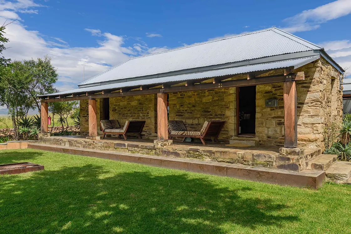 Perfect Hideaways real estate property: A small guest lodge with natural stone exterior walls and floors which form the outdoor patio, featuring zebra-patterned chairs, and a manicured lawn. Zulu Waters Game Reserve, Natal Midlands.