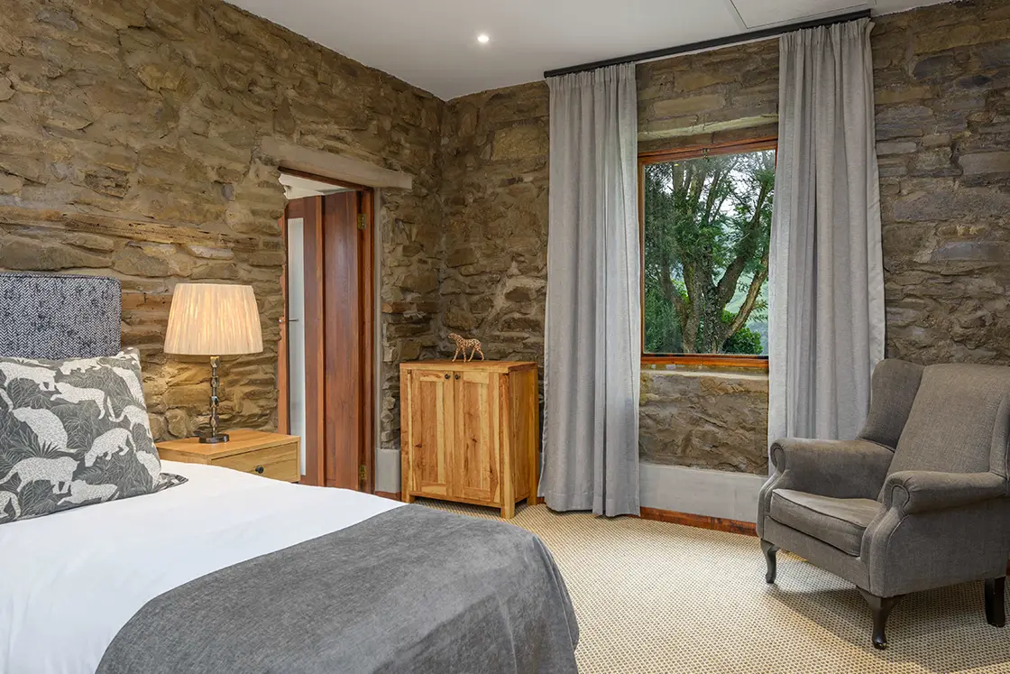 Perfect Hideaways real estate property: The corner of a bedroom with an open door to the en-suite bathroom, featuring two single beds, and natural stone interior walls. Zulu Waters Game Reserve, Natal Midlands.