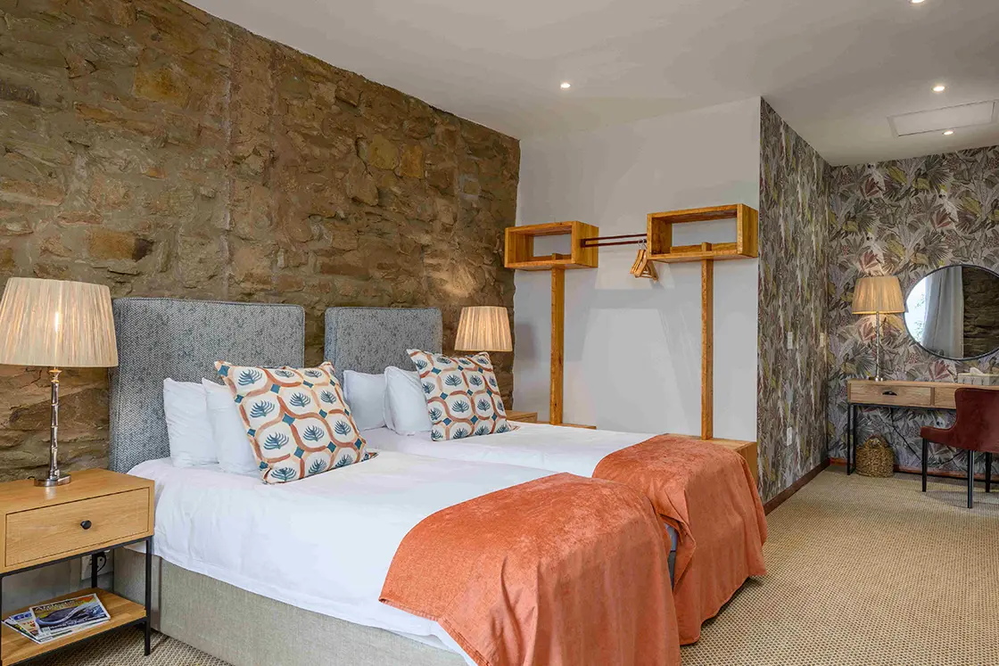 Perfect Hideaways real estate property: A bedroom area with two single beds, featuring patterned headboards, wooden furniture, floral wallpaper, and natural stone walls. Zulu Waters Game Reserve, Natal Midlands.