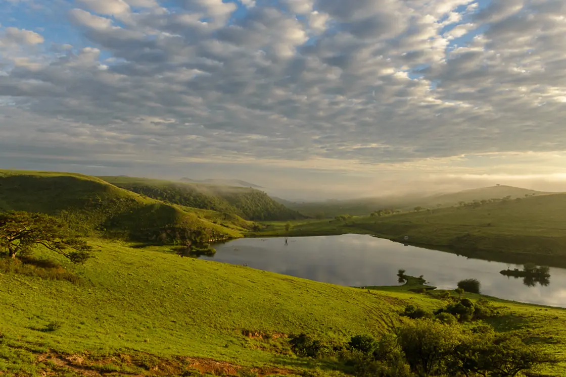 Perfect Hideaways real estate property: A scenic photograph of the lush green hills and lakes of KwaZulu-Natal, during sunset. Zulu Waters Game Reserve, Natal Midlands.