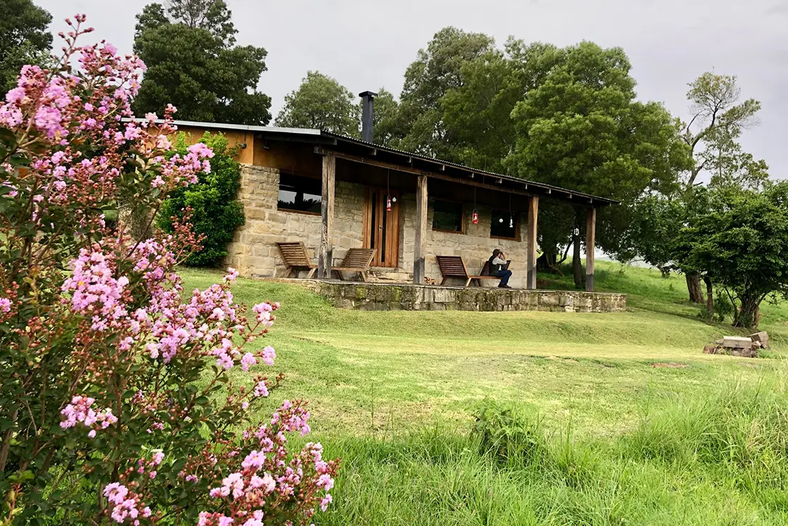 Perfect Hideaways real estate property: A small game lodge with a natural stone exterior and outdoor patio, overlooking a well-kept garden. Zulu Waters Game Reserve, Natal Midlands.