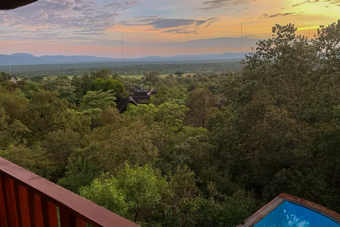 Perfect Hideaways real estate property: The view from the balcony of the game reserve, with other lodges in the foreground, mountains in the distance, and a pool directly below with the setting sky. Mabula Game Reserve, Limpopo.