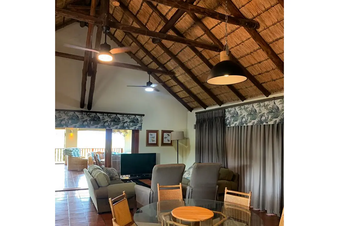 Perfect Hideaways real estate property: The lounge and living space with tropical-patterned curtain blinds, television, and a circular dining table leading out to the balcony. Mabula Game Reserve, Limpopo.