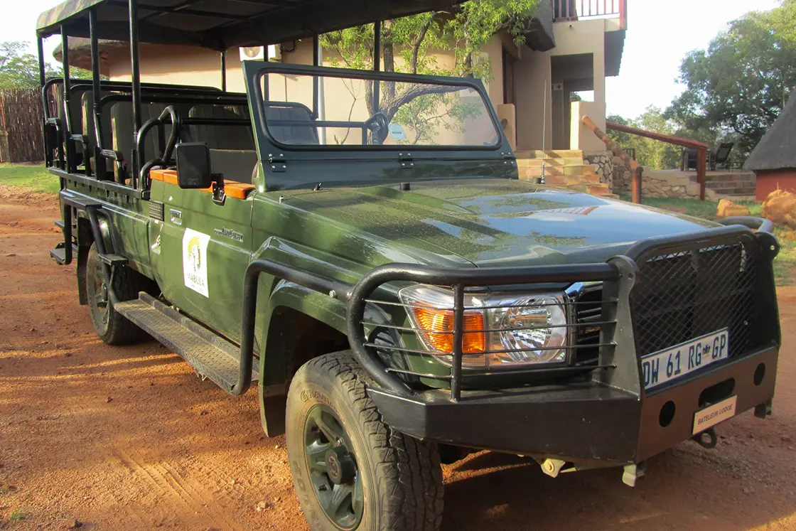 Perfect Hideaways real estate property: A green safari vehicle with plenty of seating and a canvas top, with the lodge in the background. Mabula Game Reserve, Limpopo.