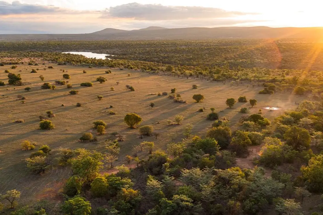 Perfect Hideaways real estate property: An aerial view of the bush and veld in the game reserve with dams and a sun setting between the mountain peaks. Mabula Game Reserve, Limpopo.