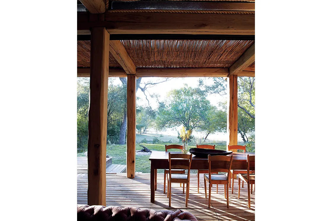 Perfect Hideaways real estate property: A wooden dining table and chairs, covered by a wooden pergola, next to a garden area. Otto House, Okavango Delta.