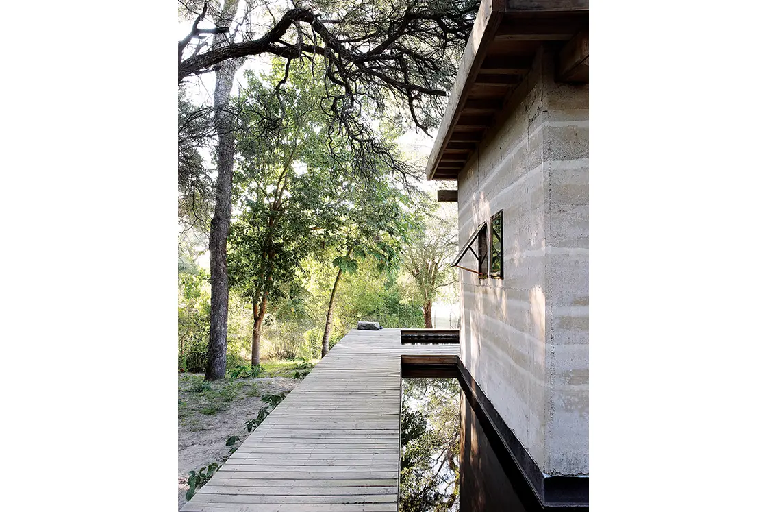 Perfect Hideaways real estate property: A rustic home in the rammed earth style, featuring a deck and a moat, surrounded by vegetation. Otto House, Okavango Delta.