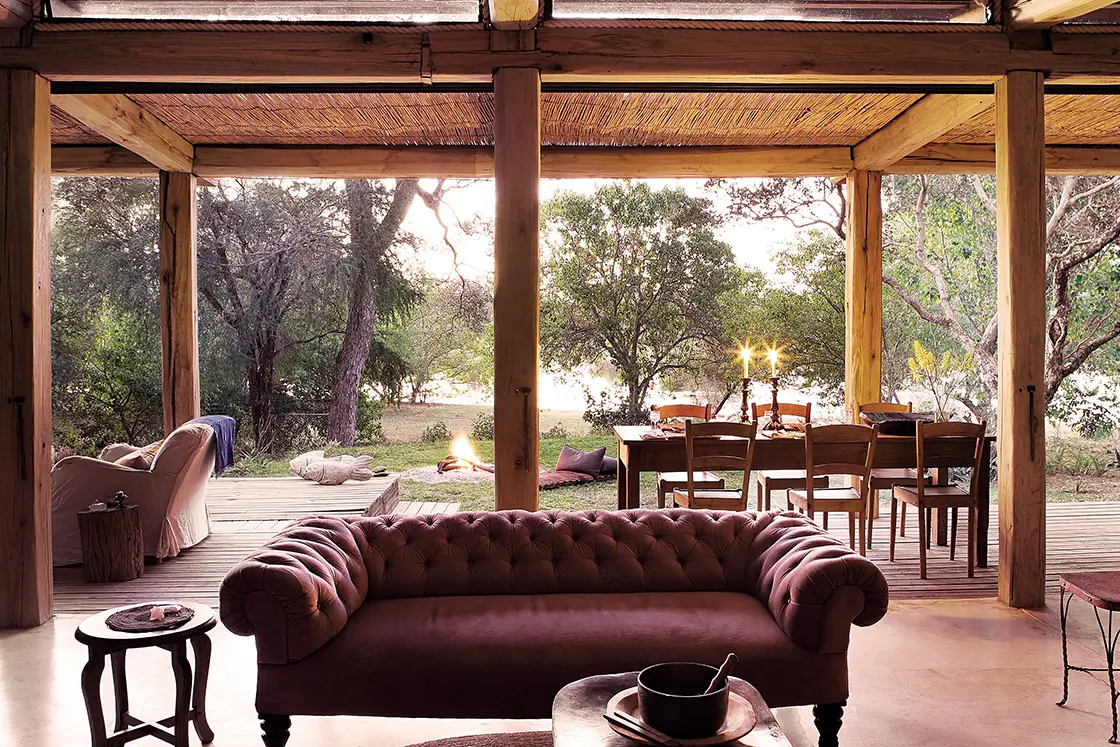 Perfect Hideaways real estate property: An open plan living area, featuring a comfortable couch, an outdoor dining area, and a fire pit in the garden. Otto House, Okavango Delta.