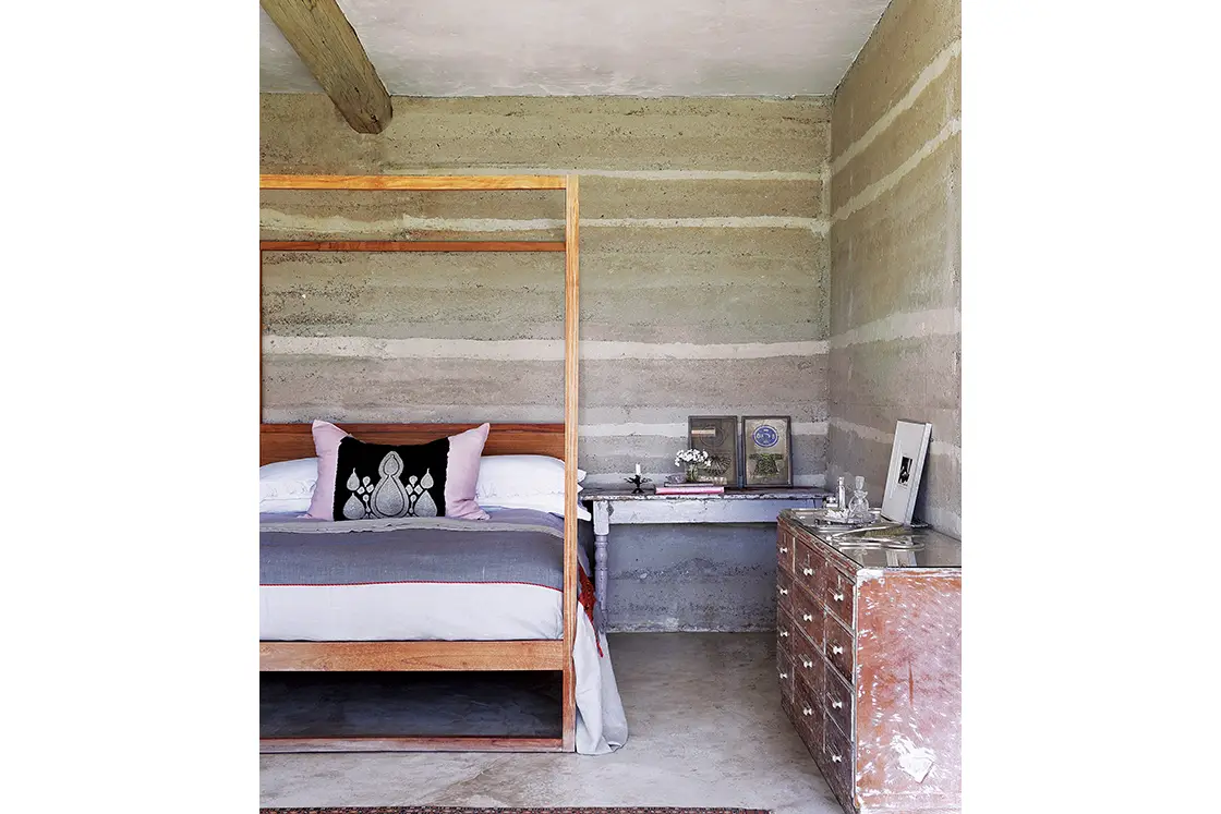 Perfect Hideaways real estate property: A bedroom with a wooden four-poster bed, rammed earth walls, and antique decor. Otto House, Okavango Delta.