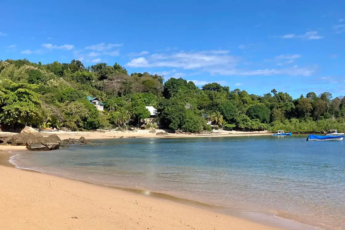 Perfect Hideaways real estate property: A picturesque stretch of beach, surrounded by lush jungle with fishing vessels in the water, and a lodge. Komba Eco Lodge, Madagascar.