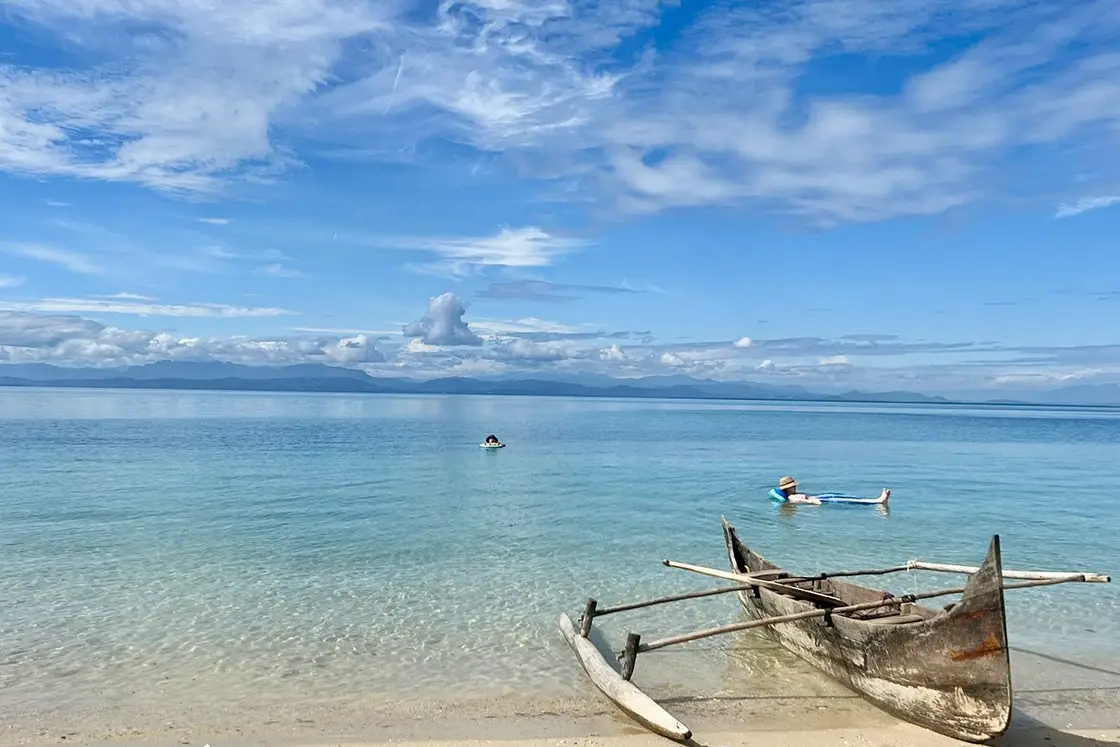 Perfect Hideaways real estate property: An ocean view, featuring a wood fishing boat on the sand, and clear blue sky. The coastline of Madagascar is visible on the horizon. Komba Eco Lodge, Madagascar.