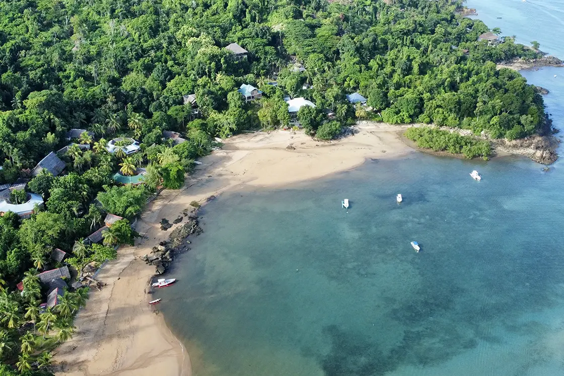 Perfect Hideaways real estate property: A sheltered bay with an eco lodge in the tree line close to the beach, some fishing vessels are anchored in the bay. Komba Eco Lodge, Madagascar.