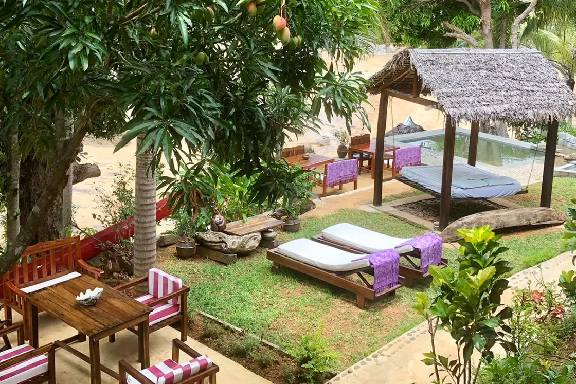 Perfect Hideaways real estate property: An outdoor dining and entertainment area, featuring a sheltered daybed and sun loungers beside a path, as well as a mango tree in the lush vegetation. Komba Eco Lodge, Madagascar.