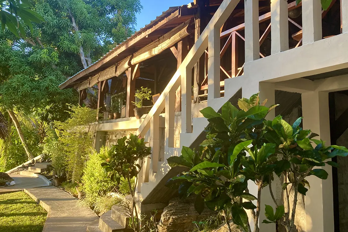 Perfect Hideaways real estate property: Steps leading up to the covered deck of a wooden eco lodge, lush green vegetation surrounds the lodge. Komba Eco Lodge, Madagascar.