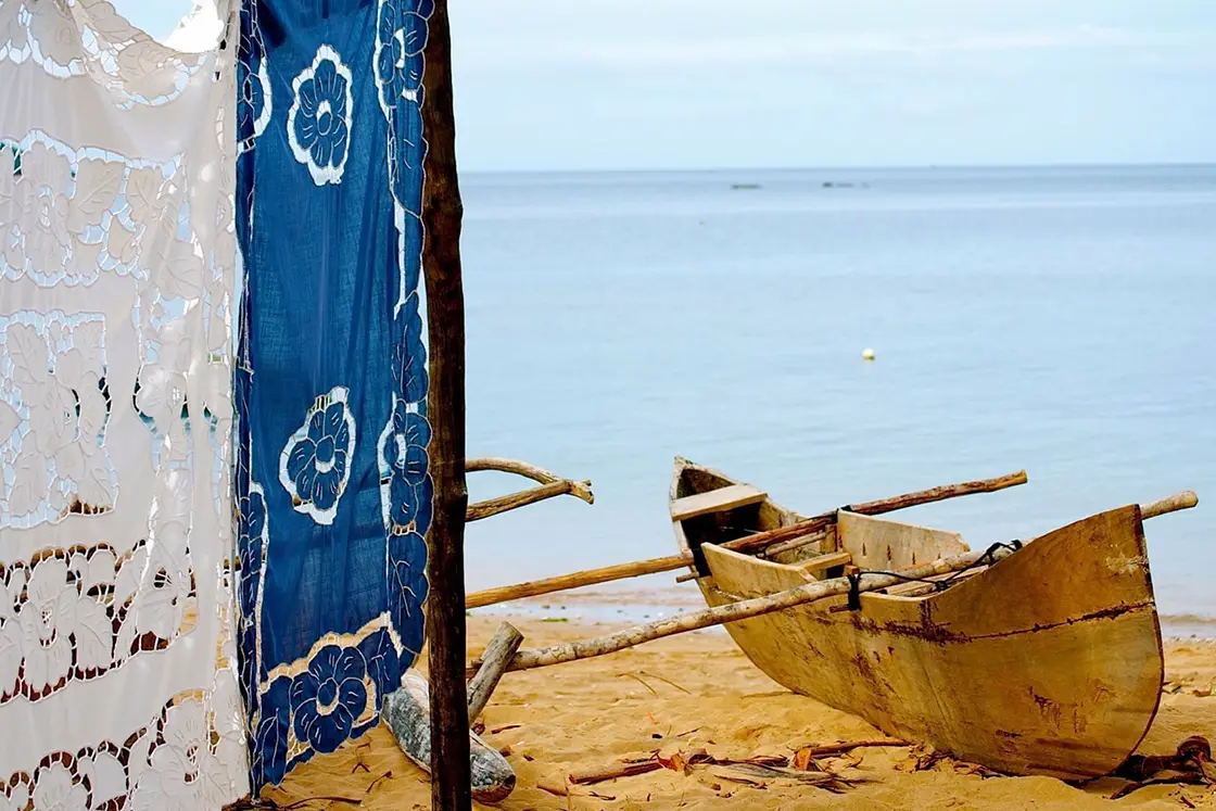 Perfect Hideaways real estate property: A traditional wooden fishing boat on sand close to blue water, and floral tapestries. Komba Eco Lodge, Madagascar.