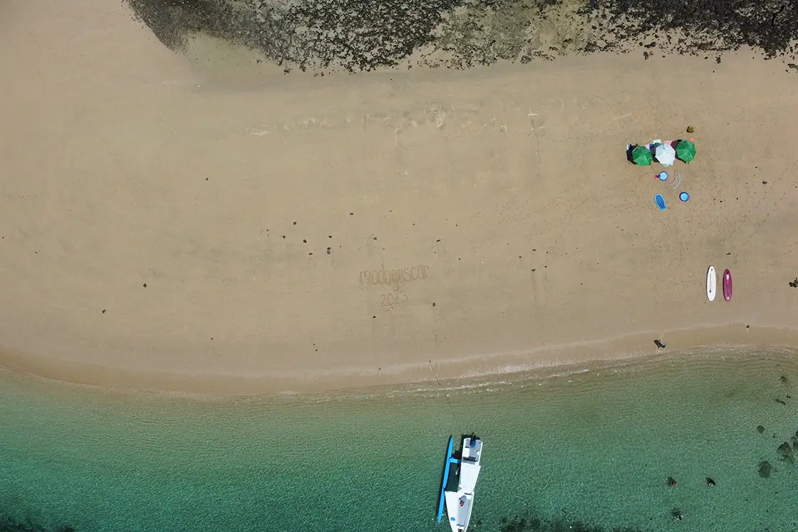 Perfect Hideaways real estate property: A bird’s eye view of a beach with umbrellas, clear water, and a nearby water taxi. Komba Eco Lodge, Madagascar.