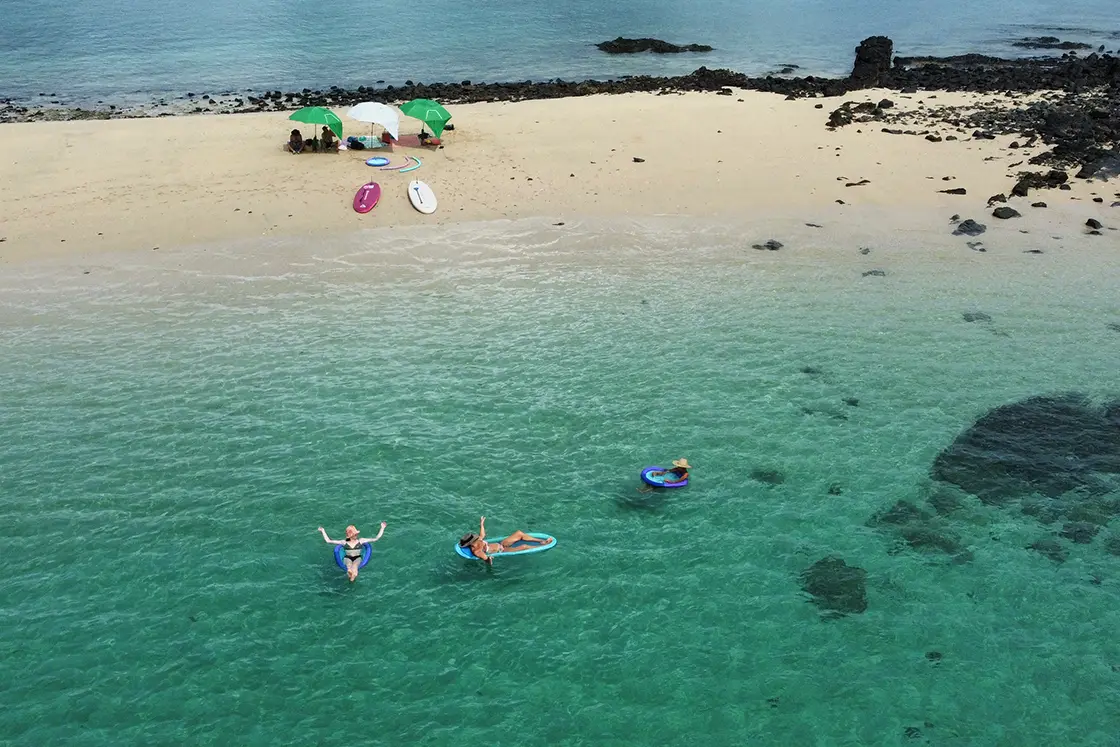 Perfect Hideaways real estate property: A small beach with umbrellas, clear blue water, and swimmers. Komba Eco Lodge, Madagascar.