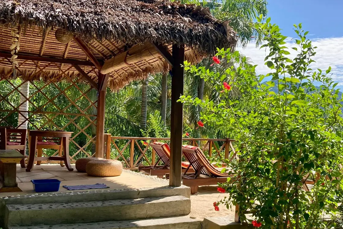 Perfect Hideaways real estate property: An outdoor shelter surrounded by tropical plants, with chairs, tables, and sun loungers. Komba Eco Lodge, Madagascar.