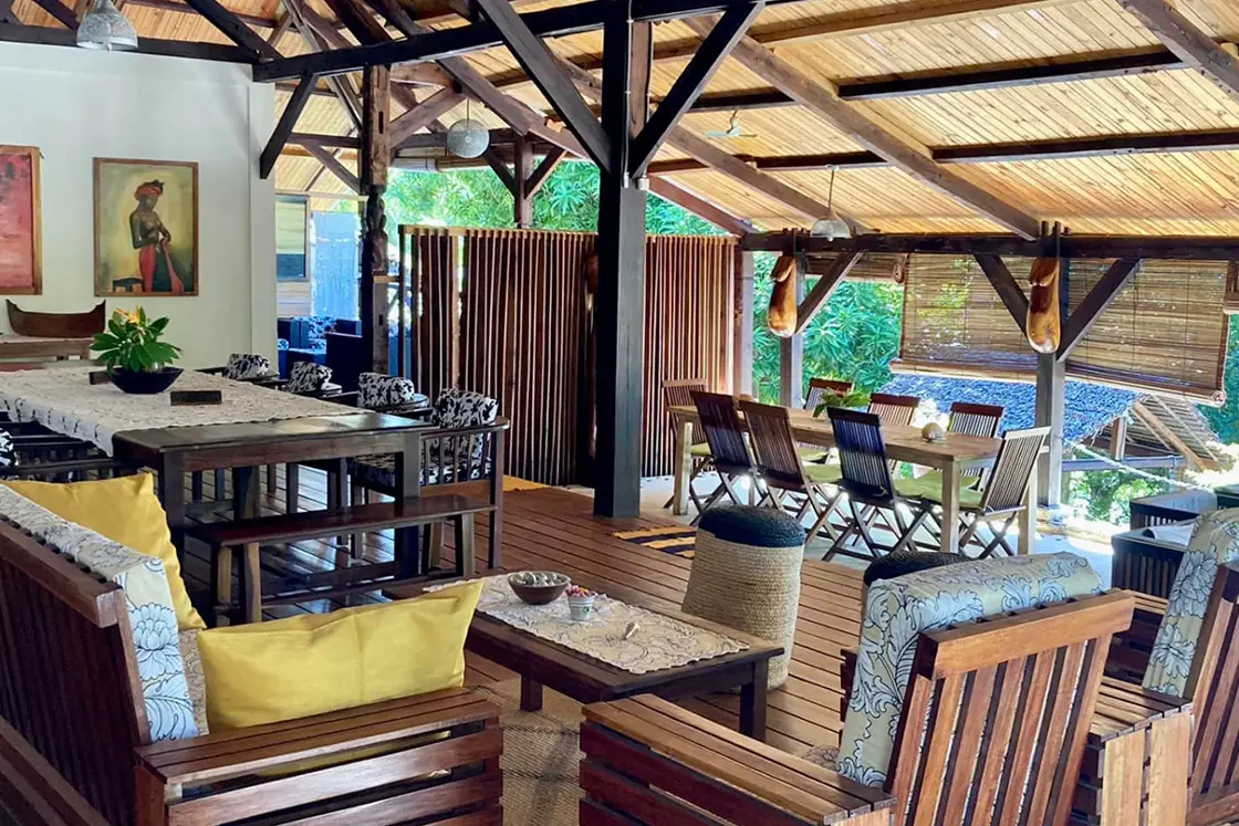 Perfect Hideaways real estate property: A covered dining area with a sloping roof and wood deck, featuring separate dining tables, and a smaller coffee table with additional chairs. Komba Eco Lodge, Madagascar.