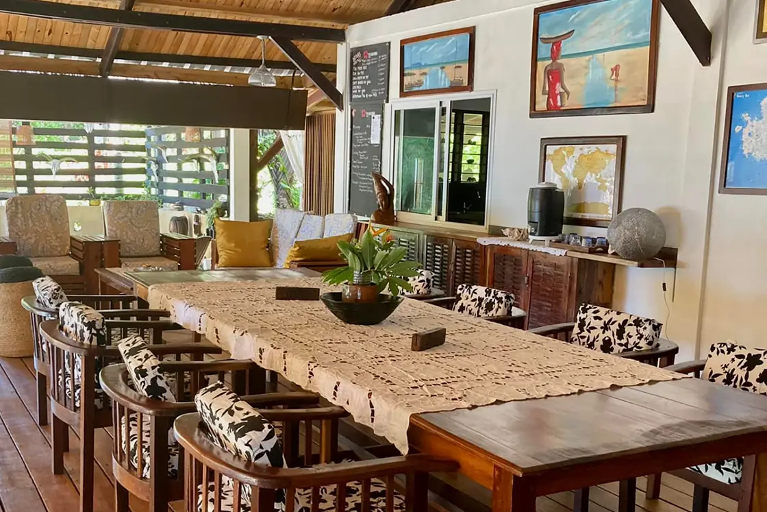 Perfect Hideaways real estate property: A covered dining area with wood floors, featuring a large dining table with black and white chairs, and rustic decor elements. Komba Eco Lodge, Madagascar.