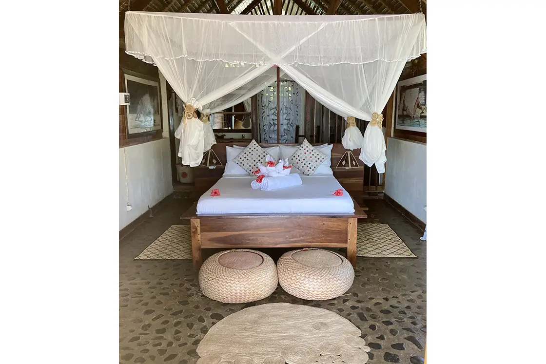 Perfect Hideaways real estate property: A bedroom area, featuring hand-made decor, a mosquito net, and a double bed on a wooden bed frame. Komba Eco Lodge, Madagascar.