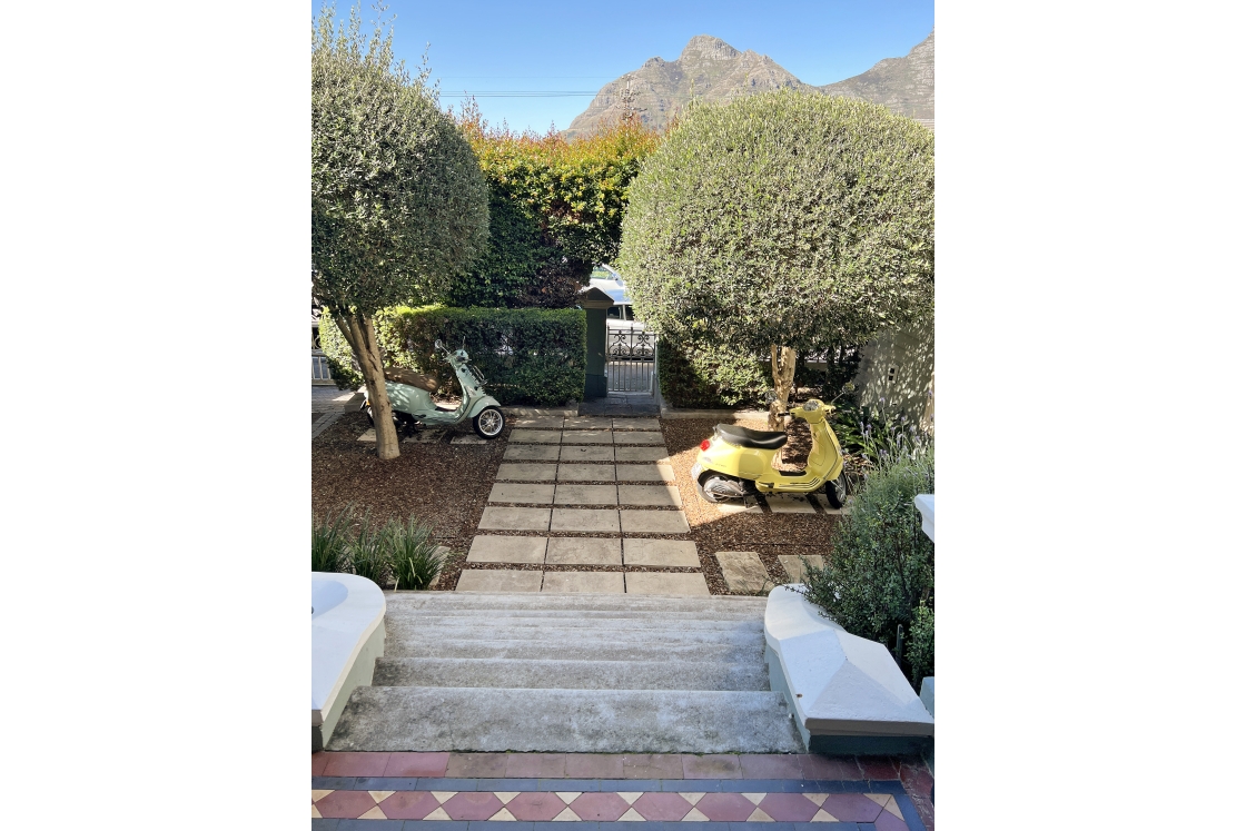 The exterior staircase looking onto the gate with two vespas parked on the stone path and a mountain peak in the distance.