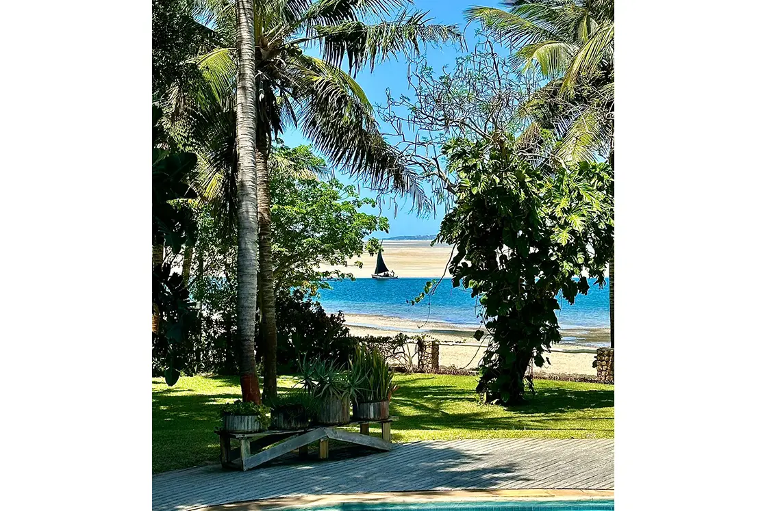 Perfect Hideaways real estate property: A lush garden at the end of the tropical guest lodge's deck, showcasing the nearby deep-water channel, and a small sailboat. Villa 1b Beach House, Vilanculos.