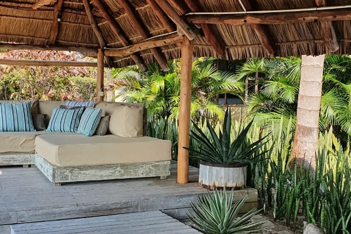 Perfect Hideaways real estate property: An outdoor deck with shade provided by the overhead gazebo, a comfortable couch with beach views, and a lush garden bordering the deck. Villa 1b Beach House, Vilanculos.